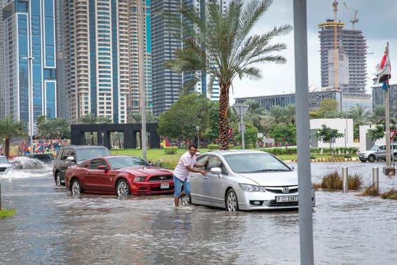 Pessoas empurrando carros para fora da água em ruas alagadas de Dubai.