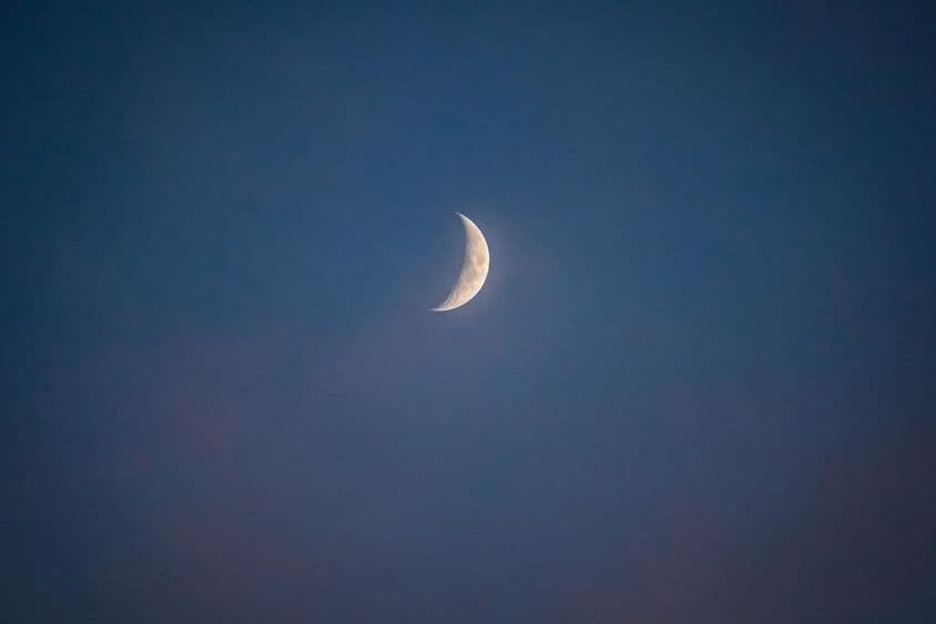 Lua crescente ao anoitecer com nuvens sussurrantes.