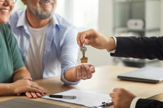 Um agente imobiliário entregando chaves para um casal idoso sorridente.