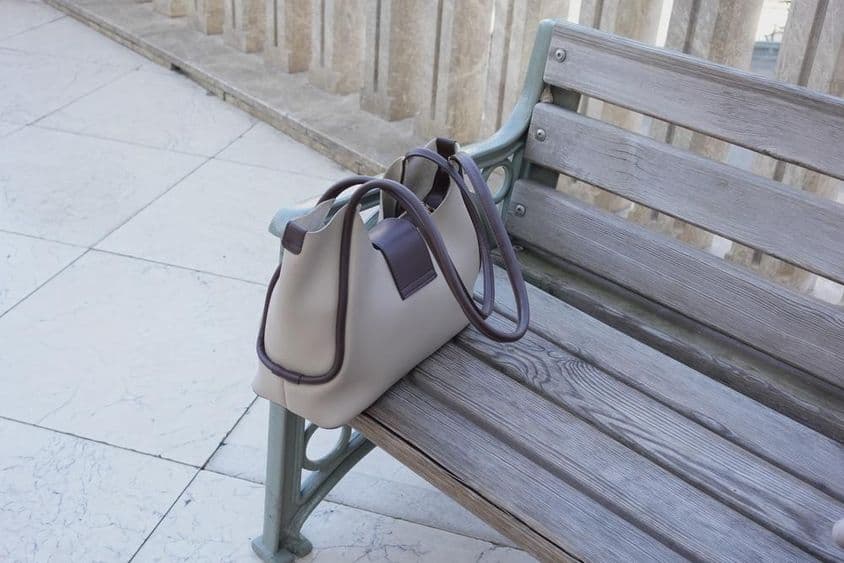 Bolsa repousando em um banco de madeira em ambiente urbano.