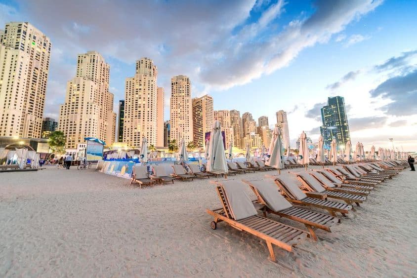 Pôr do sol na Marina Beach, Dubai, com cadeiras de praia e arranha-céus.