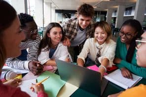 Um grupo alegre de estudantes universitários sentados à mesa olhando para um caderno.