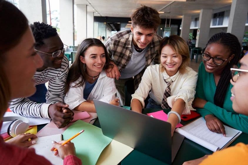 Um grupo alegre de estudantes universitários sentados à mesa olhando para um caderno.