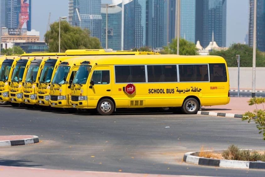 Uma fila de ônibus escolares amarelos em Dubai estacionados do lado de fora.