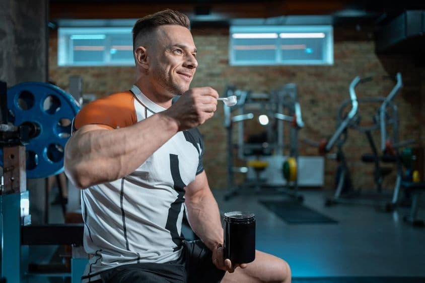 Fisiculturista musculoso com corpo perfeito segurando proteína na academia.