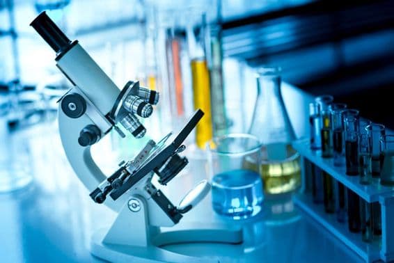 Microscópio em uma mesa com tubos químicos e vidraria.