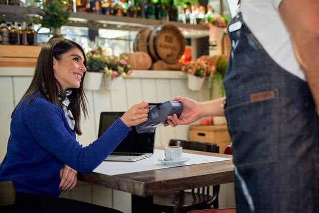 Mulher de cabelo castanho sentada em um café, pagando com cartão de crédito.