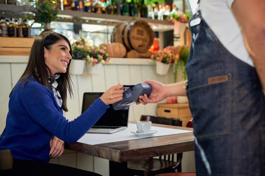 Mulher de cabelo castanho sentada em um café, pagando com cartão de crédito.