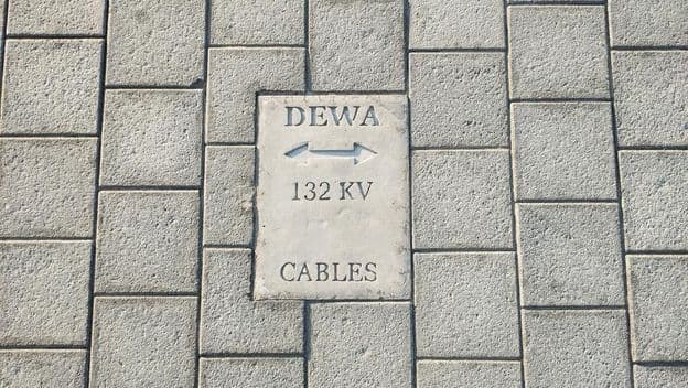 Placa avisando de cabos no chão de pedras em Dubai.