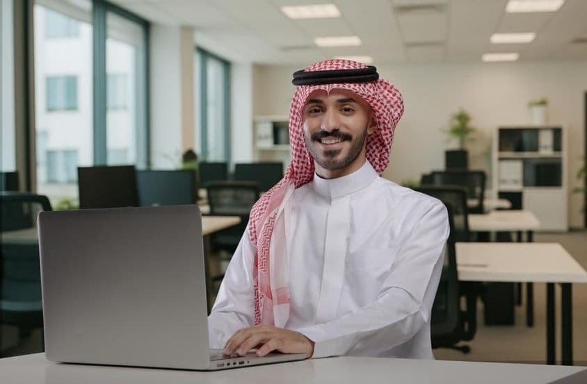 Homem árabe sorridente em traje tradicional trabalhando.