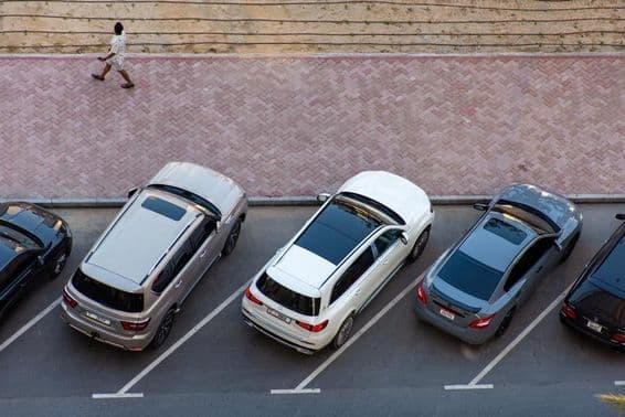 Vista aérea de carros estacionados em Dubai e um homem caminhando em uma calçada pavimentada.