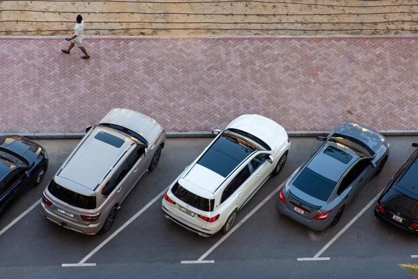 Vista aérea de carros estacionados em Dubai e um homem caminhando em uma calçada pavimentada.