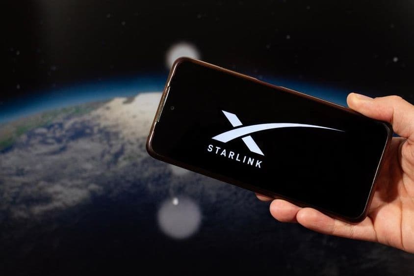 A mão de um homem segurando um smartphone com o logotipo da Starlink na mão direita.