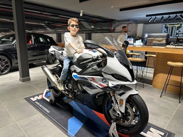 Menino de óculos escuros sentado em uma motocicleta BMW.