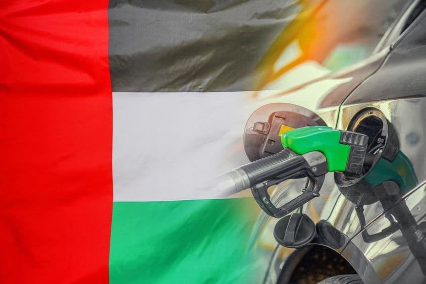 Carro em um posto de combustível com bandeira dos Emirados Árabes Unidos ao fundo.