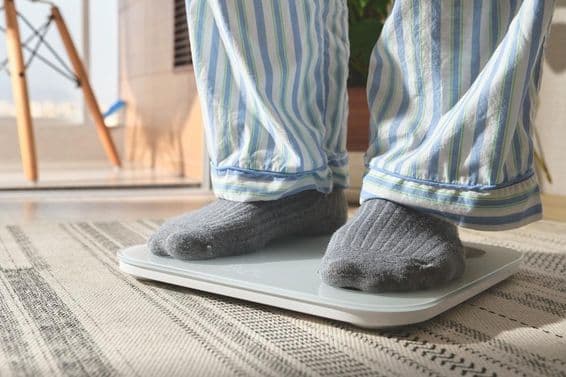 Homem de pijama listrado em pé em uma balança digital branca.