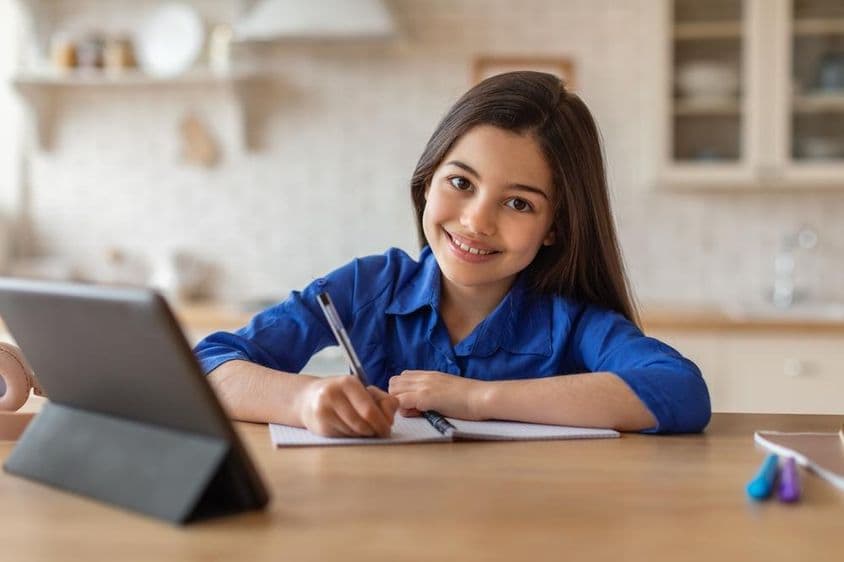 Menina escolar feliz participando de aulas de casa usando um tablet.