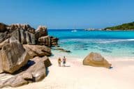 Dois viajantes caminhando nas areias brancas macias da Praia Anse Cocos em Seychelles.