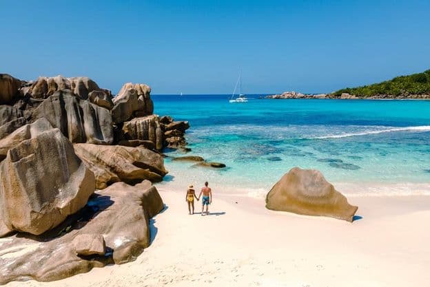 Dois viajantes caminhando nas areias brancas macias da Praia Anse Cocos em Seychelles.