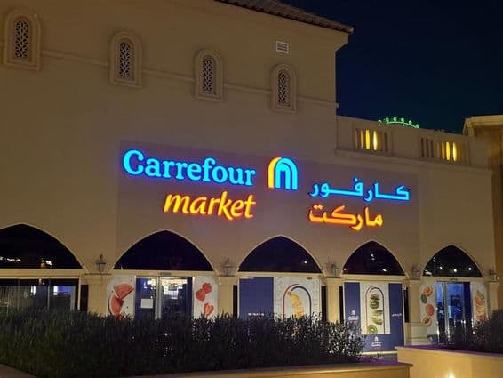 Logotipo iluminado do mercado Carrefour com nome da marca em árabe