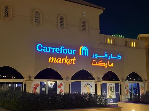 Logotipo iluminado do mercado Carrefour com nome da marca em árabe