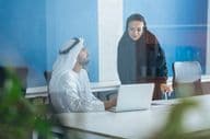 Um homem e uma mulher em trajes tradicionais trabalhando em um escritório empresarial em Dubai.