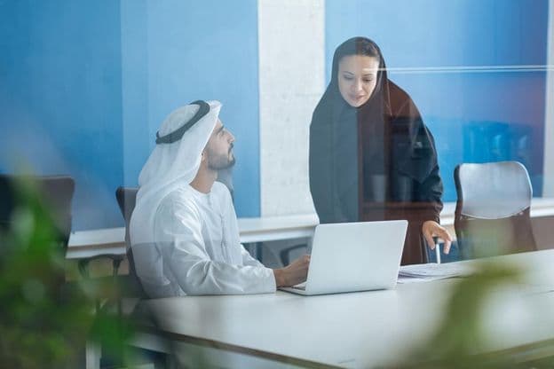 Um homem e uma mulher em trajes tradicionais trabalhando em um escritório empresarial em Dubai.