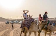 Turistas andando de camelo no deserto.