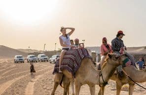 Turistas andando de camelo no deserto.