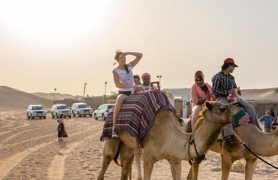 Turistas andando de camelo no deserto.