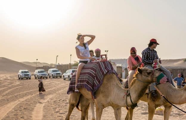 Turistas andando de camelo no deserto.