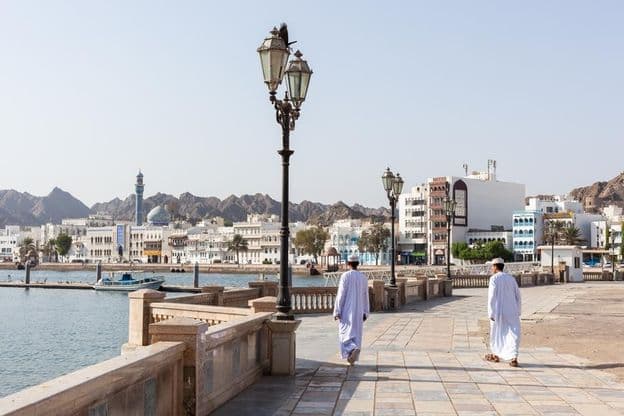 Homens em trajes tradicionais omanenses ao longo da orla de Mascate.