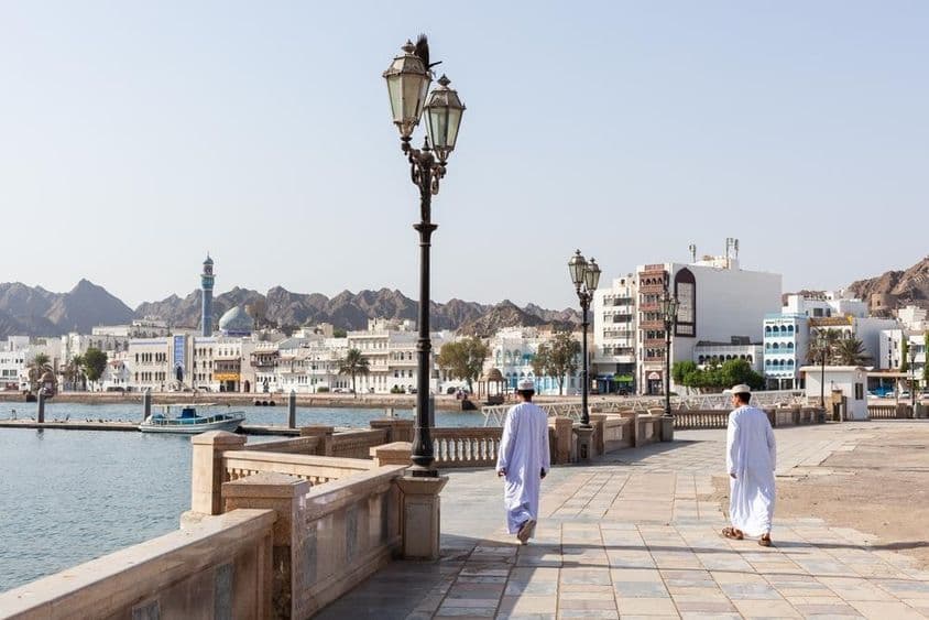 Homens em trajes tradicionais omanenses ao longo da orla de Mascate.