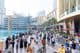Uma multidão diversificada de turistas e locais caminha ao longo da movimentada promenade à beira-mar em frente ao Dubai Mall.